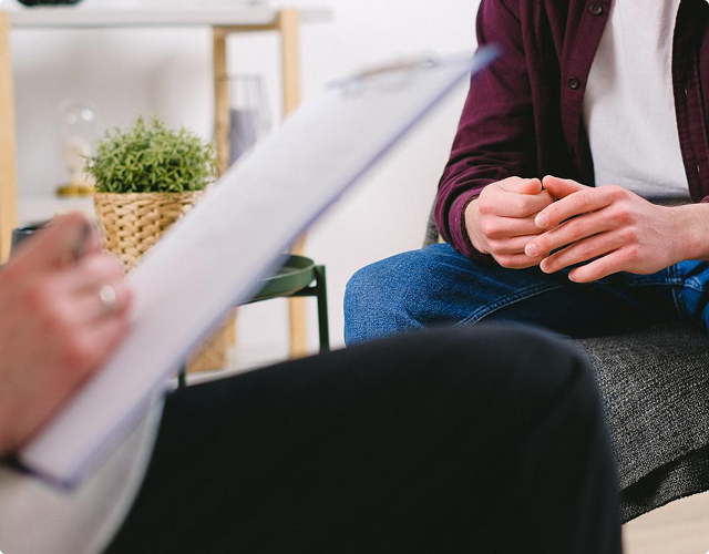 Photo anonyme d'un psychologue prenant des notes de ce que lui transmet son patient. L'angle s'arrête à la main du psychologue et au buste du patient.
